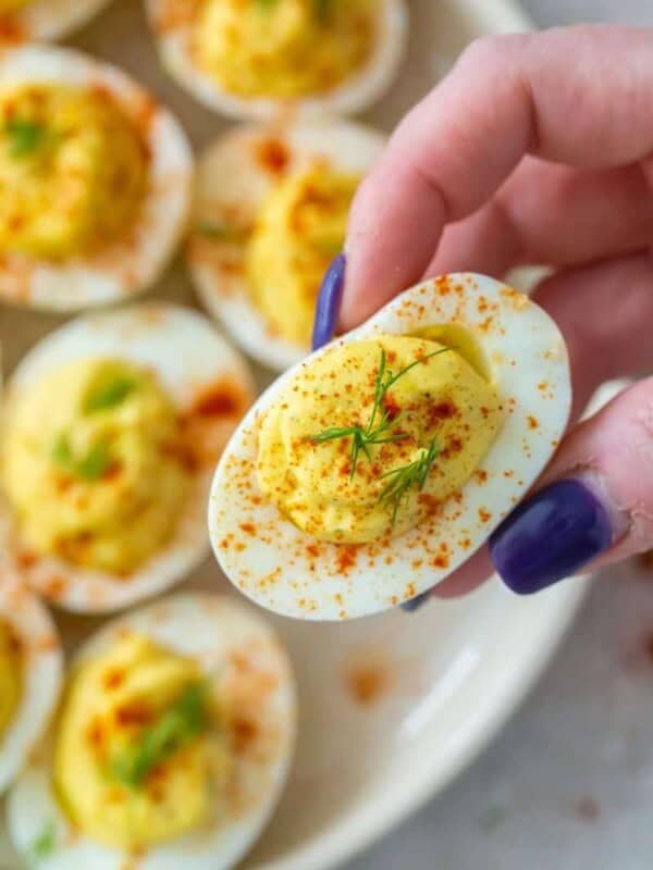 Hand grabbing a deviled egg without vinegar from plate
