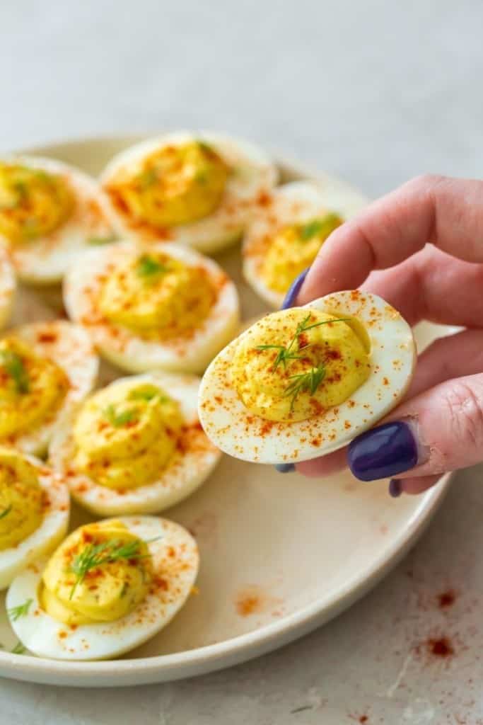 hand grabbing a vinegar-free deviled egg from plate