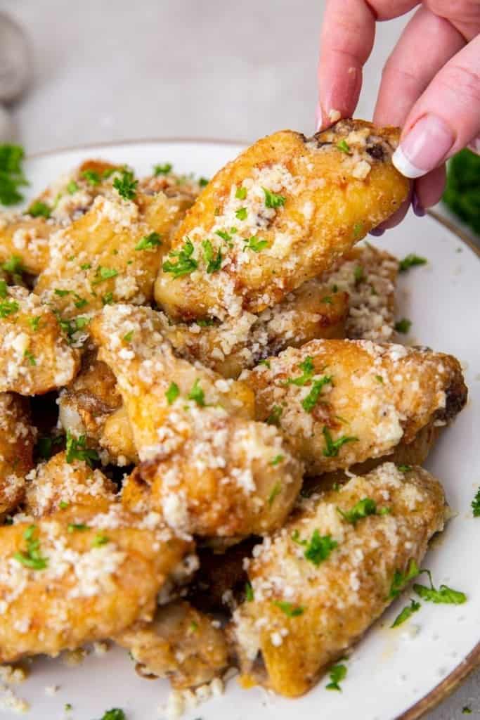 hand grabbing a garlic parmesan wing off white plate