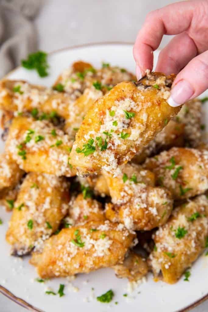 Hand reaching for one of many garlic parmesan wings on plate