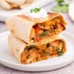 Chicken Fajita Wrap cut in half stacked on a white plate with a dollop of sour cream on top