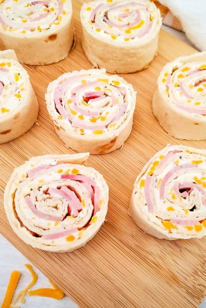 cutting board with ham and cheese roll-ups spaced out