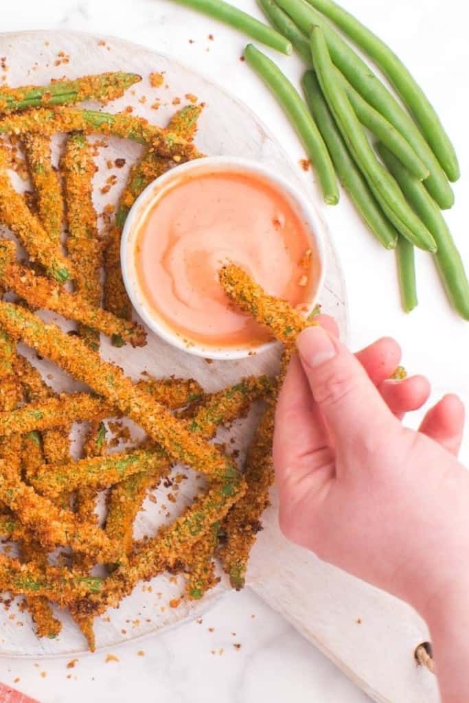 Hand dipping air fryer green bean fry in sauce
