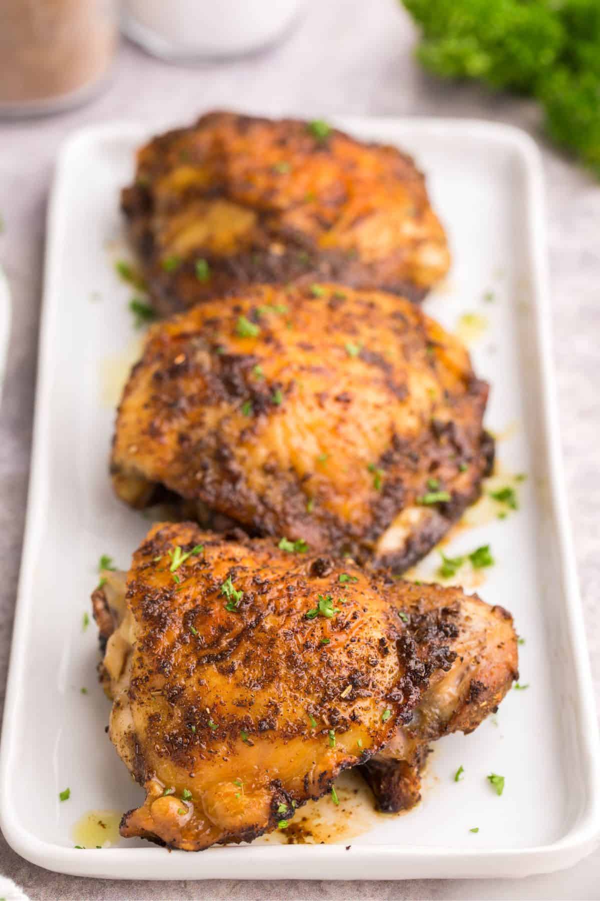 Air fryer bone in chicken thighs on a rectangular white platter about to be served.
