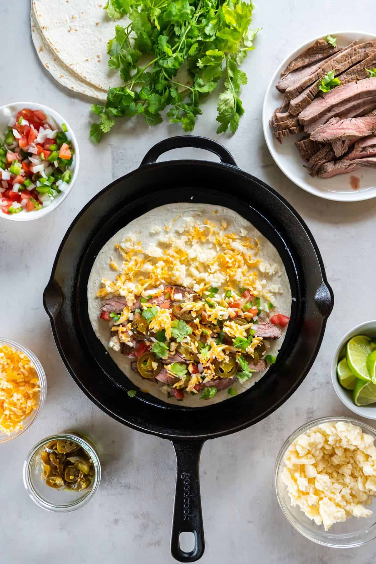 Tortilla on a cast-iron skillet with cheese the toppings piled on one side and cheese on both sides.