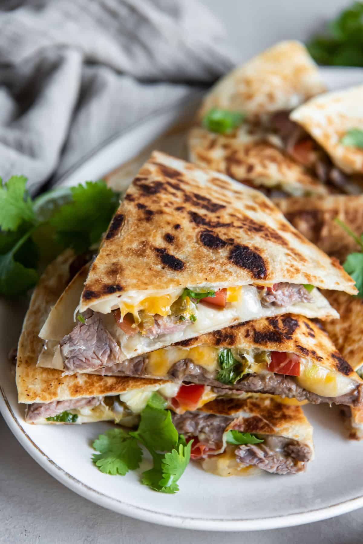 Carne asada quesadilla slices stacked on top of each other on a white plate.