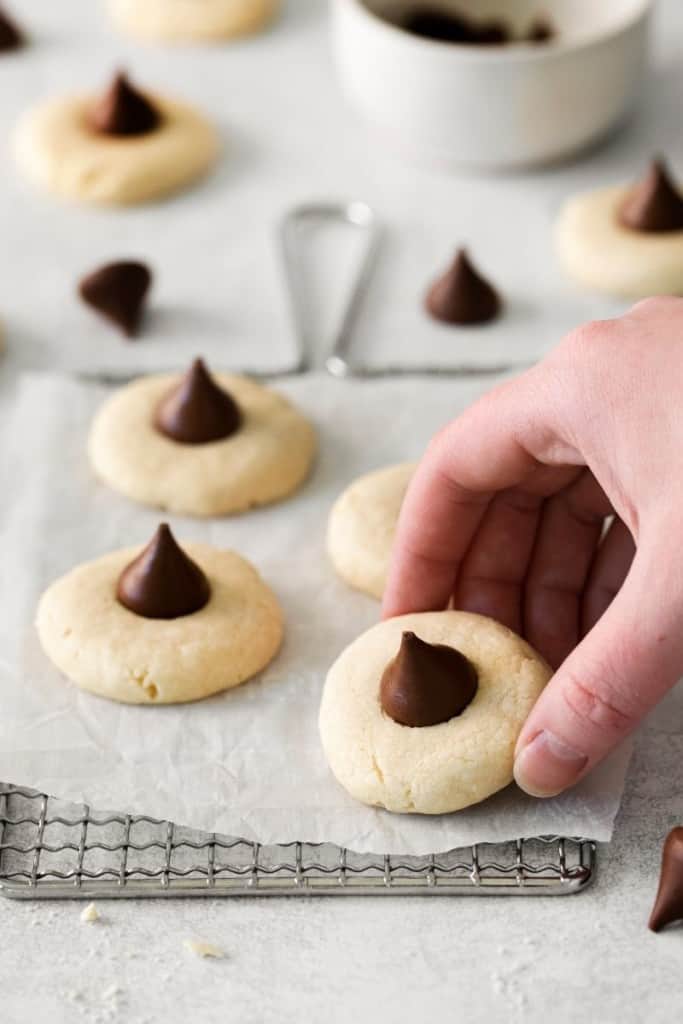 a hand picking up a sugar cookie with hershey kiss from parchment paper