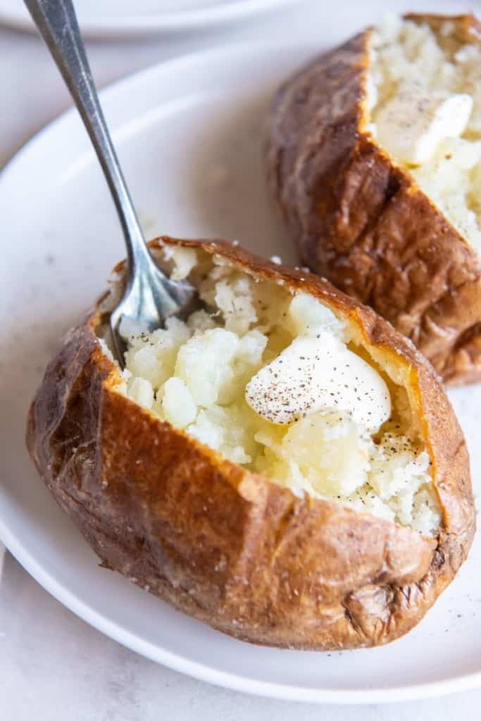 air fryer baked potatoes on a plate with a fork in one of them
