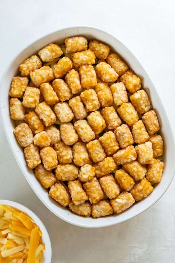 Tater tots added to the tater tot casserole ready to be baked in the oven.
