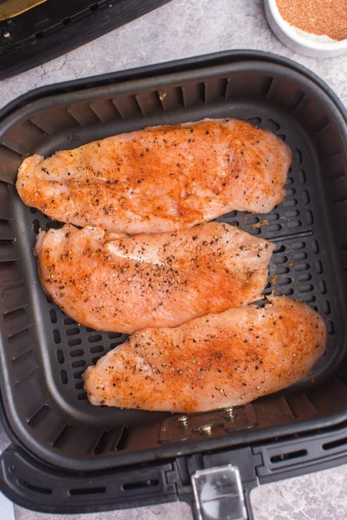 Raw chicken breasts in an air fryer basket.