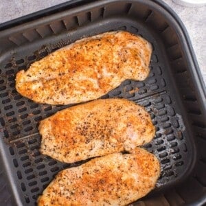 Cooked grilled chicken in an air fryer basket.