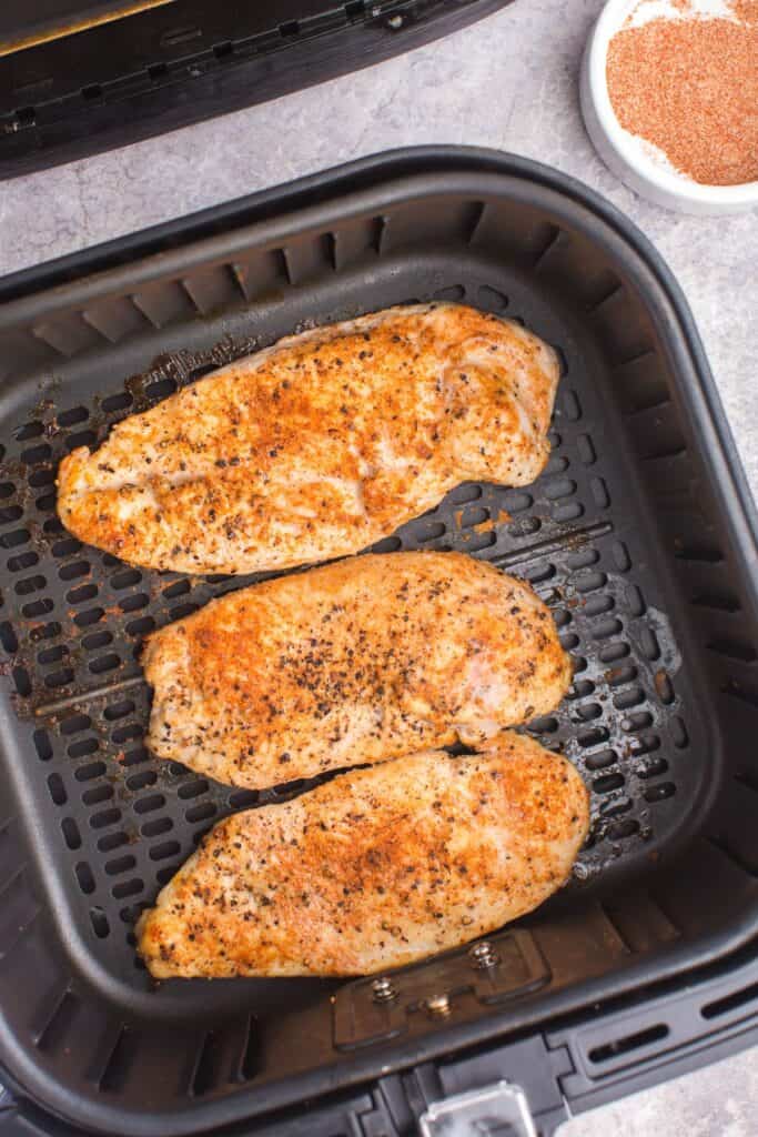 Cooked grilled chicken in an air fryer basket.