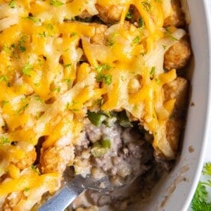 Overhead view of tater tot casserole with green beans with a serving spoon inside and a scoop missing.
