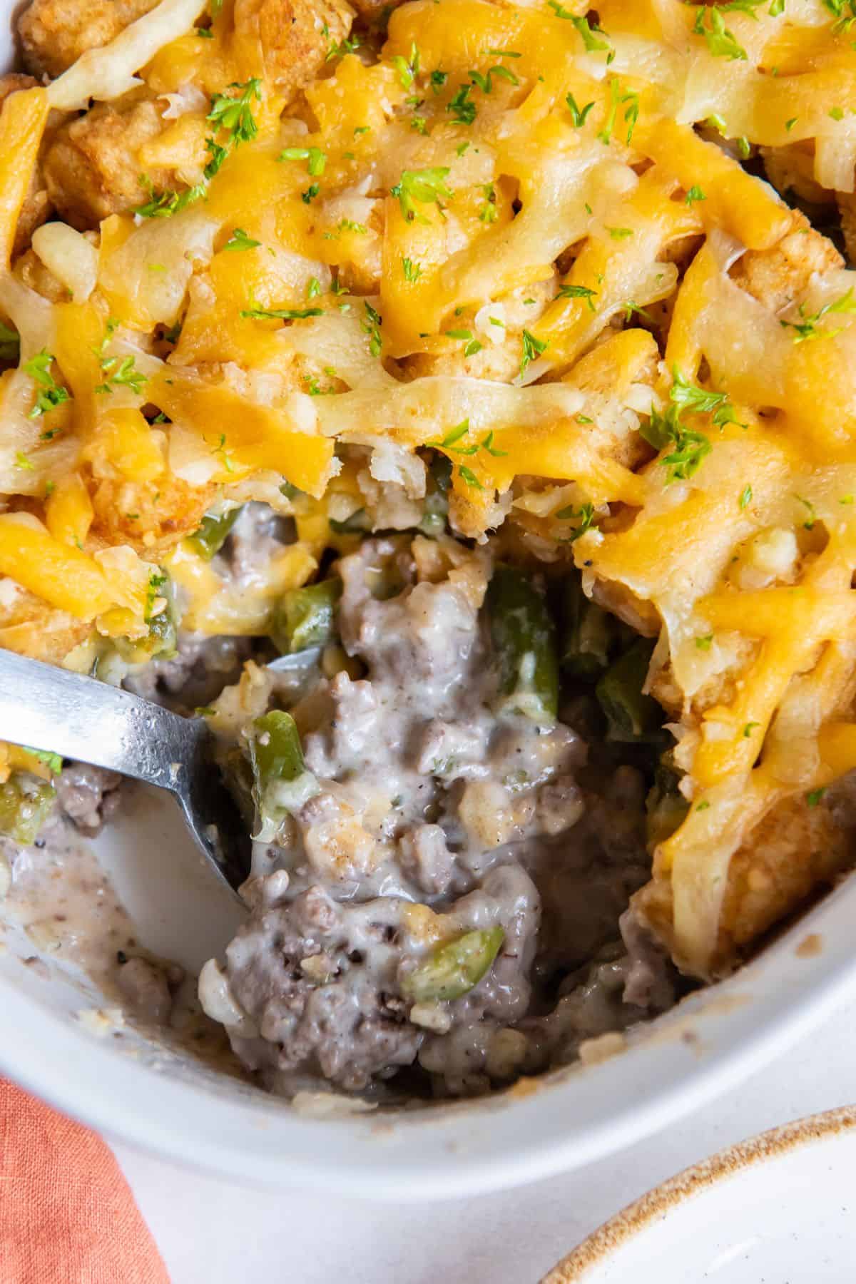 Close up of the tater tot casserole with ground beef so you can see the inside of it with serving spoon scooping a little up.