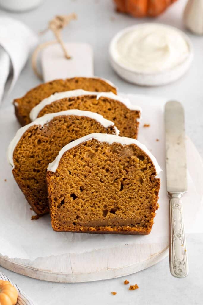Pumpkin bread with cream cheese sliced and placed on a plate with a knife next to it. 