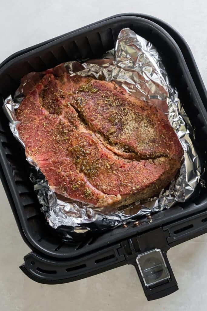 Raw chuck roast in the air fryer with aluminum foil.