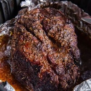 Cooked chuck roast in an air fryer basket with foil and juices around it.