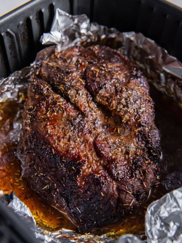 Cooked chuck roast in an air fryer basket with foil and juices around it.