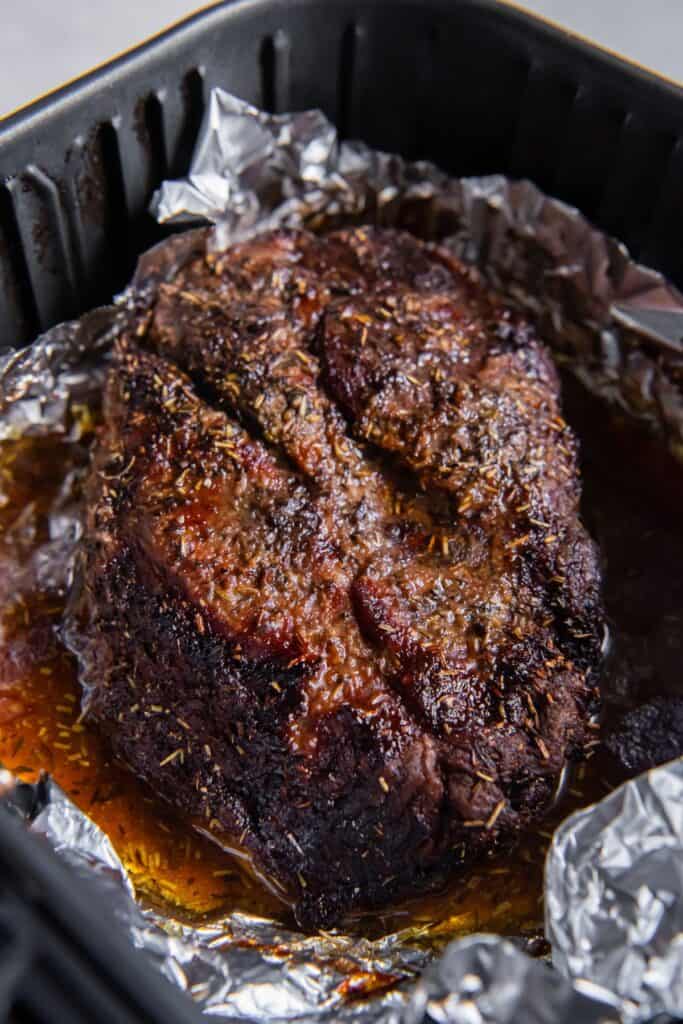 Cooked chuck roast in an air fryer basket with foil and juices around it.