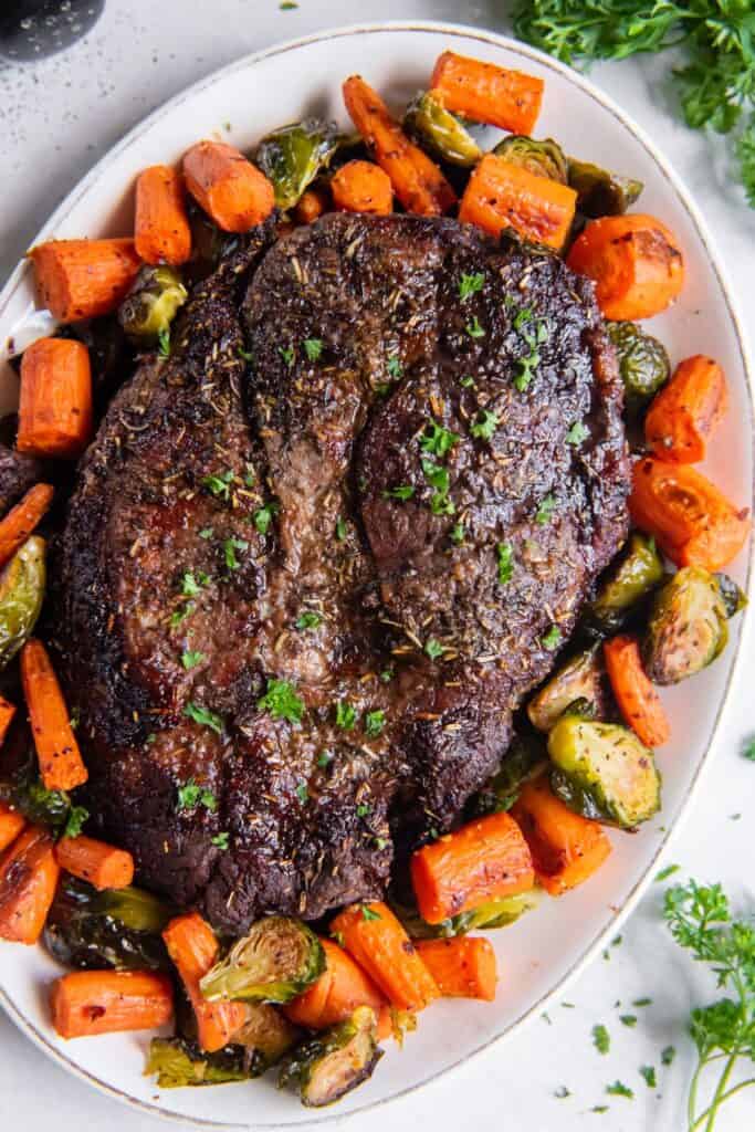 Whole air fryer chuck roast with carrots and brussels sprouts surrounding it.