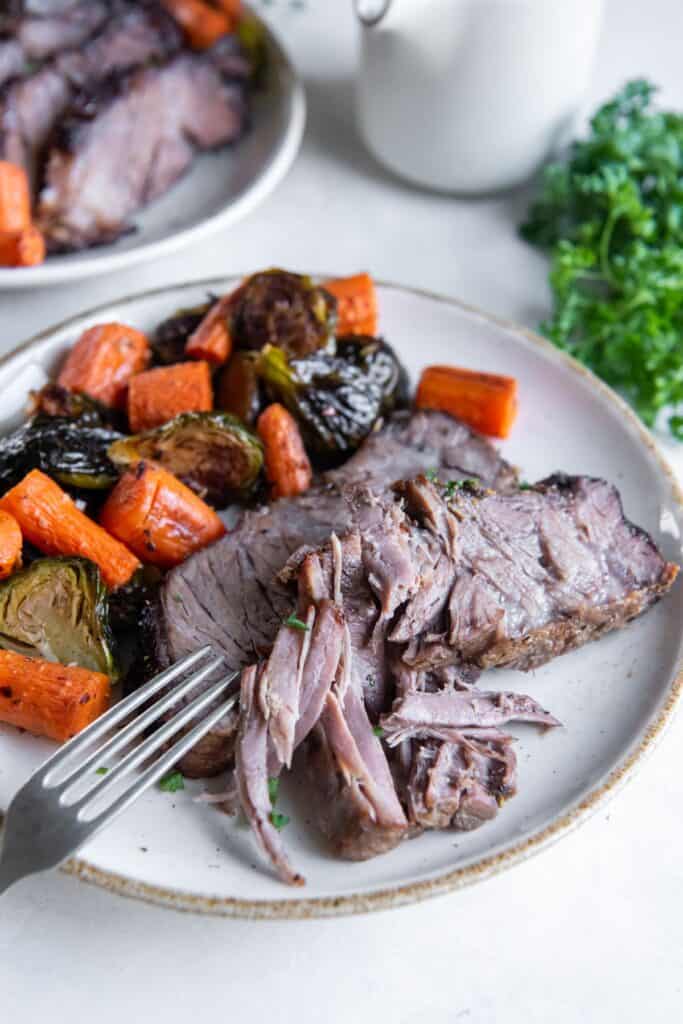 A slice of chuck roast on a plate with a fork that pulled a piece from it.