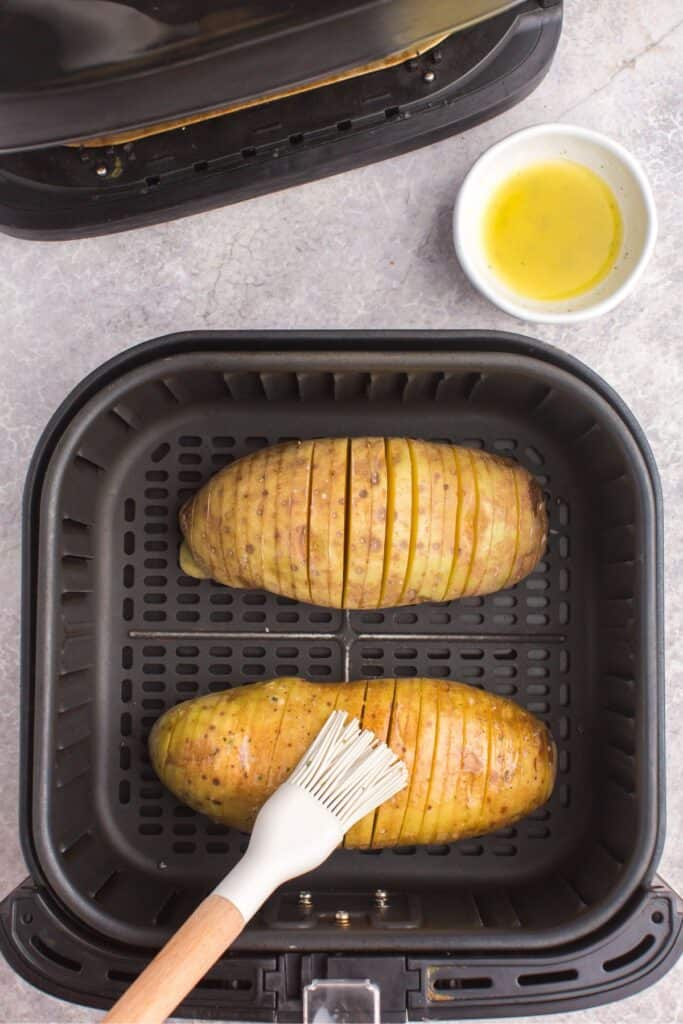 Raw cut potatoes in the air fryer ready to be air fried and being basted with butter and ranch seasoning.