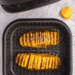 Two cooked hasselback potatoes in an air fryer basket with the cheese melted.