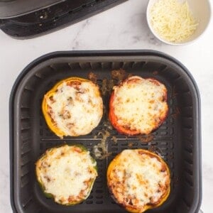 Cooked stuffed peppers in an air fryer basket with browned melted cheese on top.