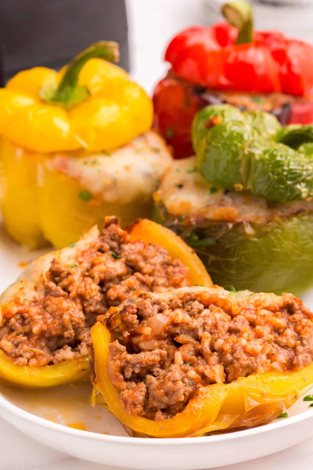 Air fry stuffed peppers on a serving plate with one cut in half to see the inside of it.