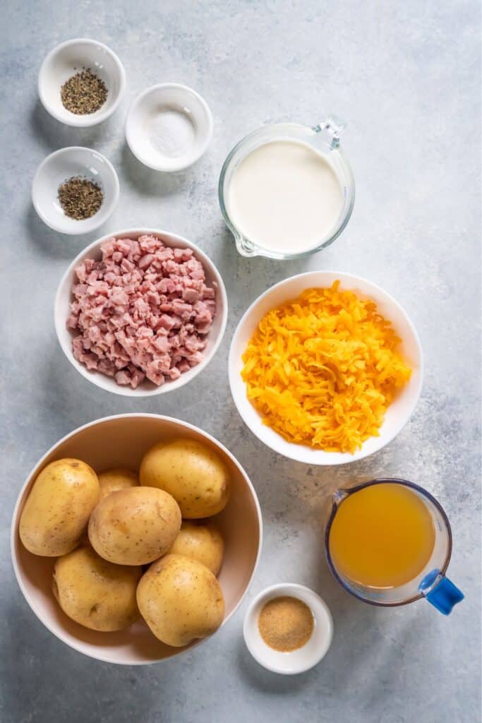 Ingredients needed to make instant pot scalloped ham and potatoes: yukon gold potatoes, chicken broth, heavy cream, cheddar cheese, ham, garlic powder, thyme, salt, and pepper.