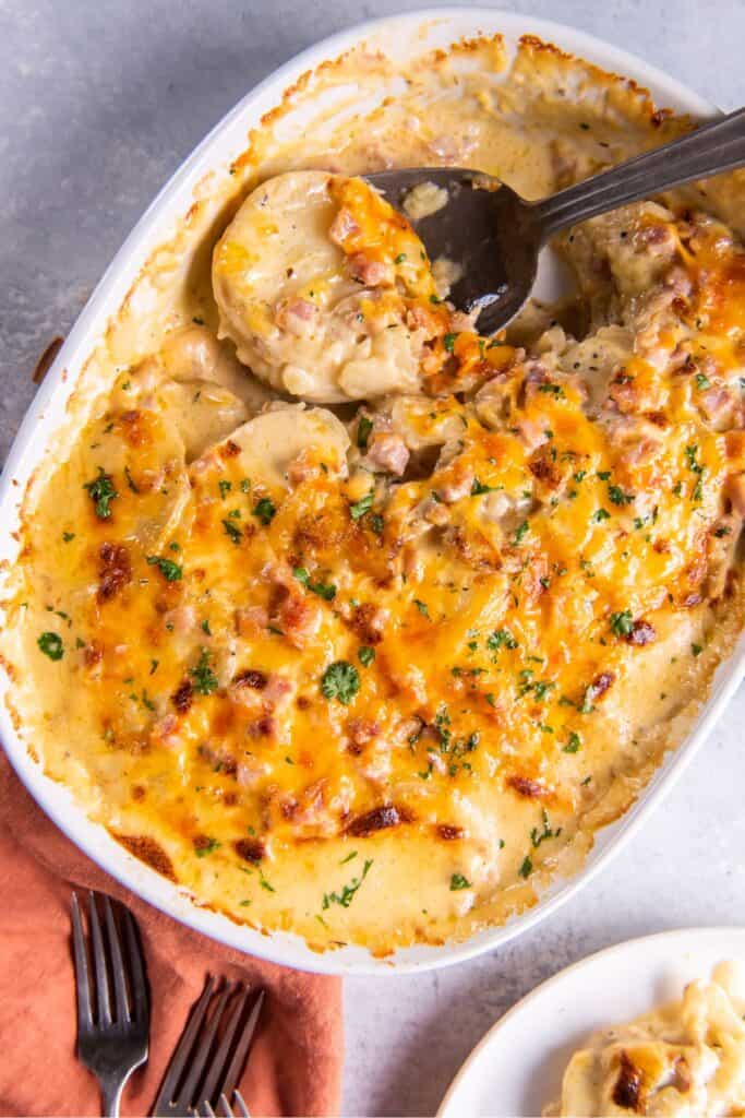 Instant pot scalloped potatoes and ham in a baking dish with a spoon in it.