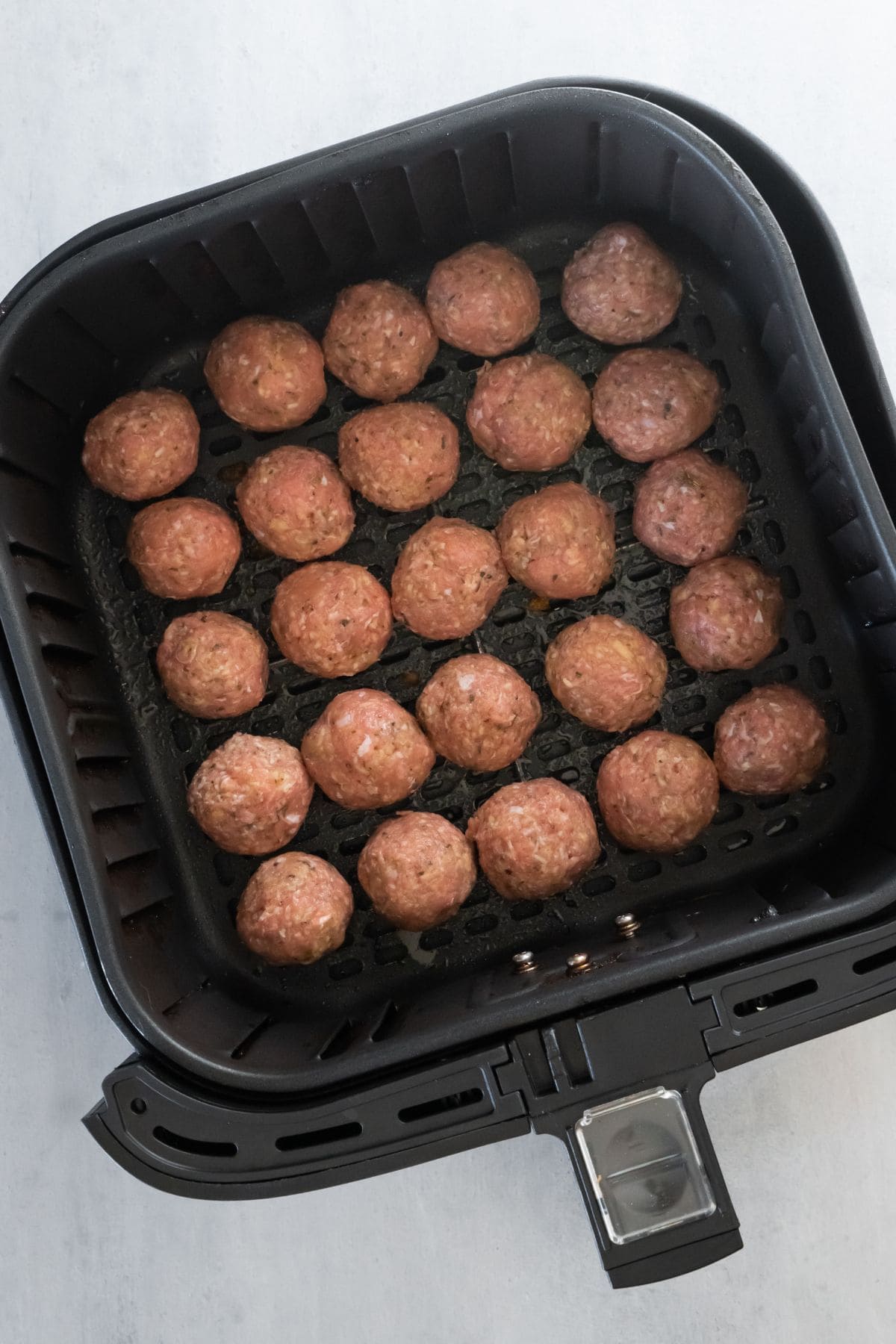 Raw turkey meatballs in an air fryer basket.