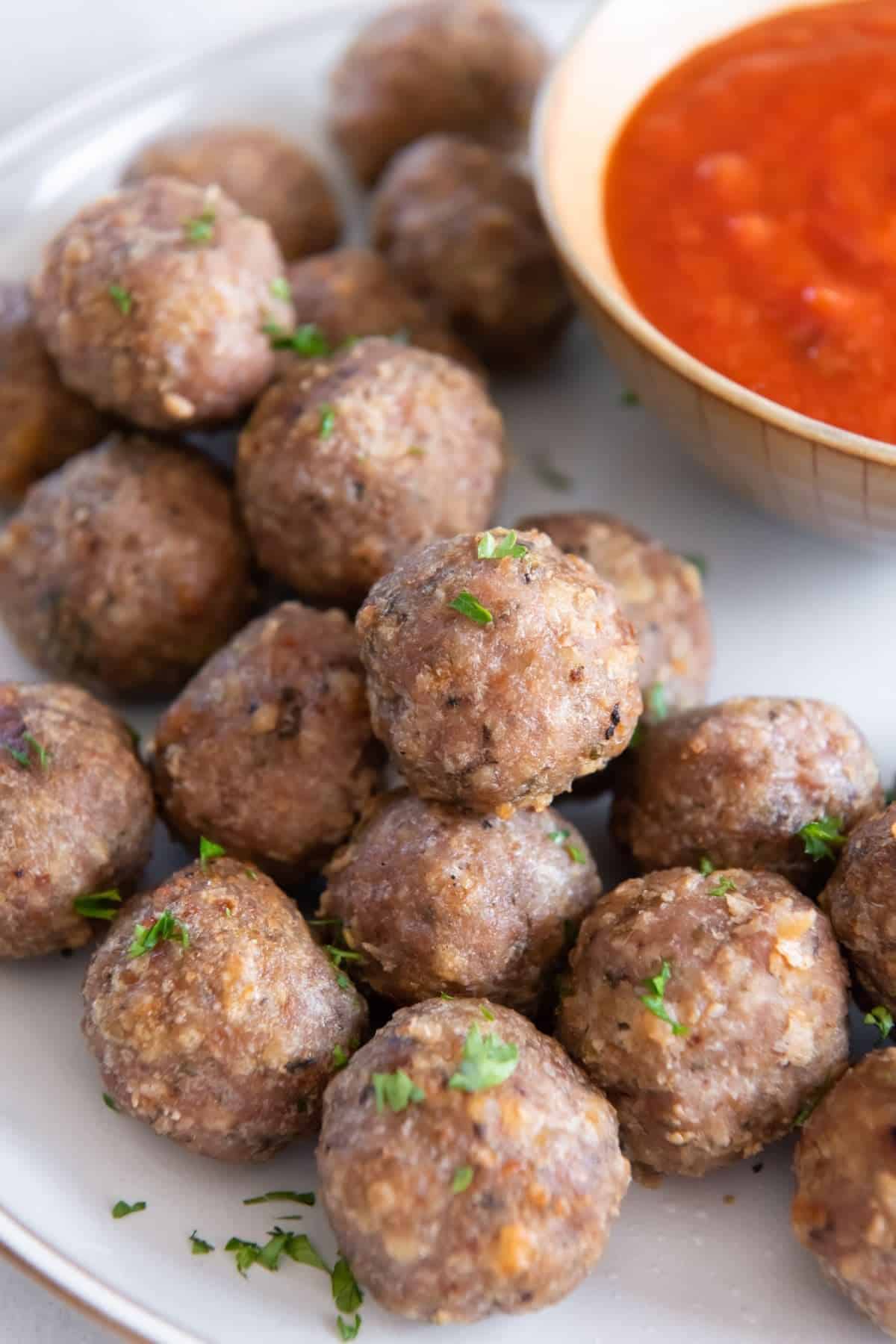 Air fryer turkey meatballs on a plate with tomato sauce on the side.