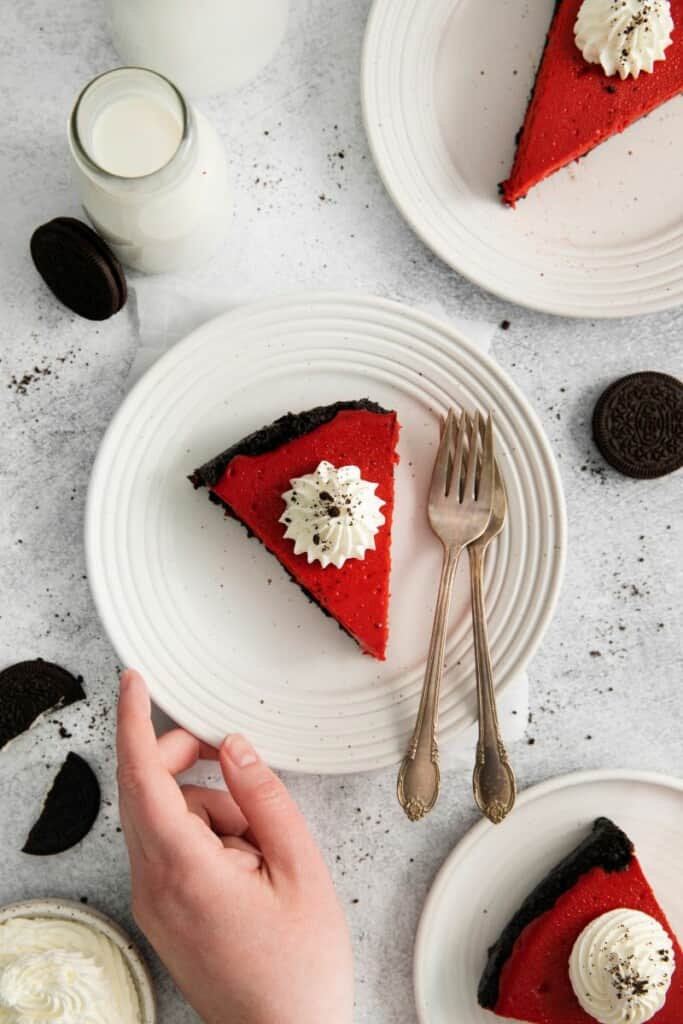 Slice of cheesecake on a plate with a hand grabbing it