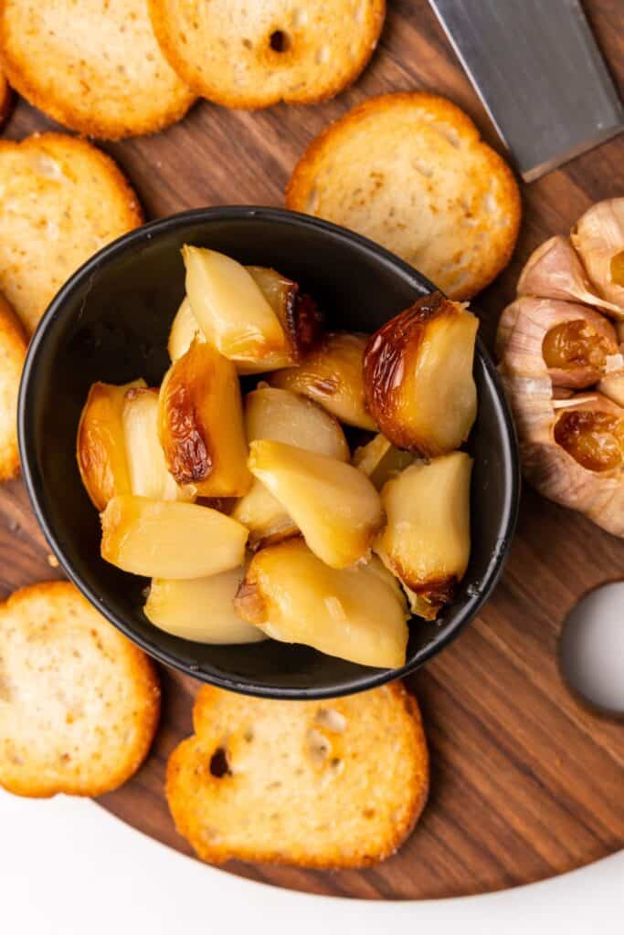 Air fryer roasted garlic peeled out of the shells, served in a bowl with crostini pieces to be spread on top of them.