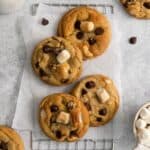 Chocolate chip marshmallow cookies on a counter with parchment paper and a wired rack.