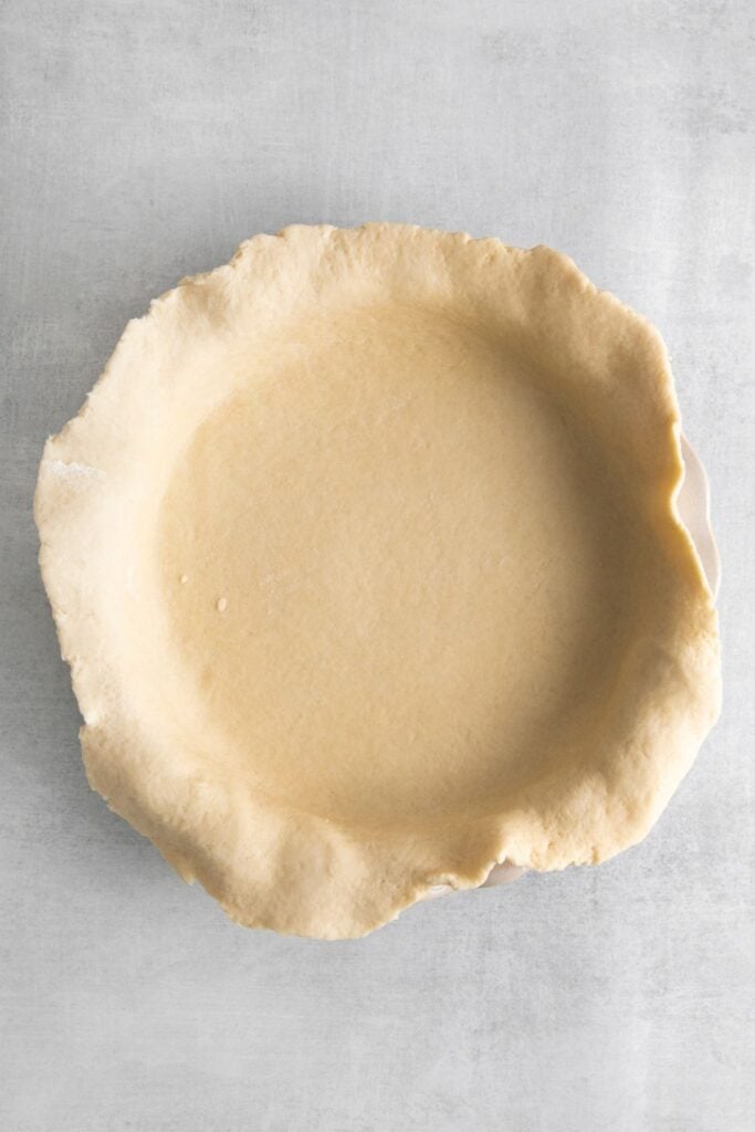 Rolled out simple pie crust over a pie dish about to be pressed down to fit it.