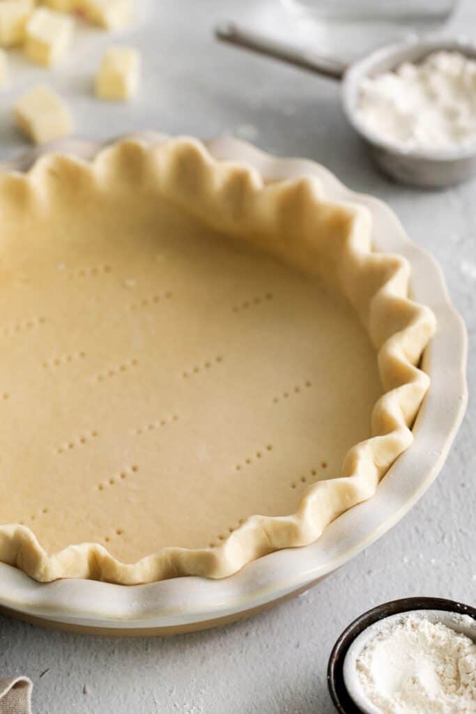 Side view of the simple pie crust recipe in a pie pan with edges crimped and fork holes in the bottom.