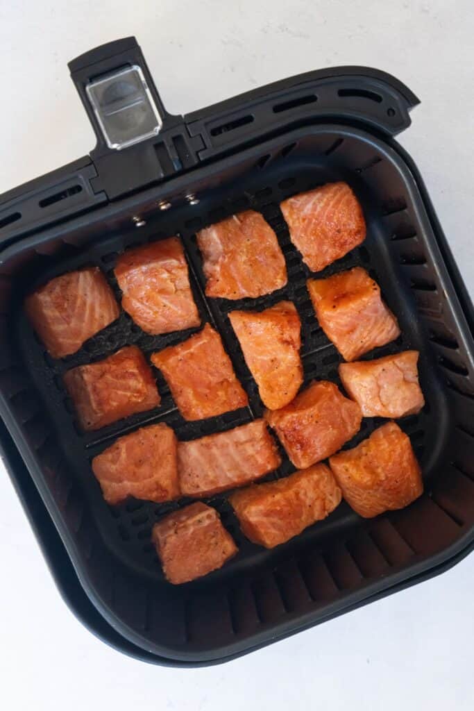 Raw salmon bites in an air fryer basket.