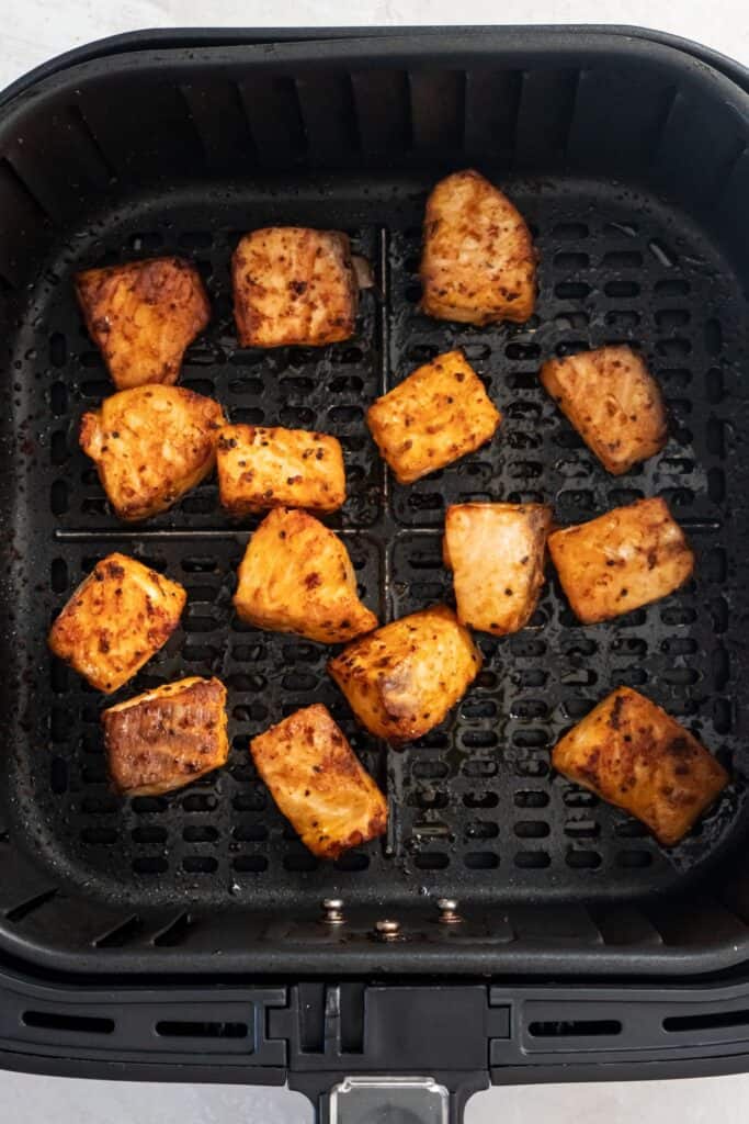 Cooked salmon bites in an air fryer basket.