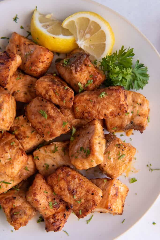 Air fried salmon bites on a white plate with lemon wedges.