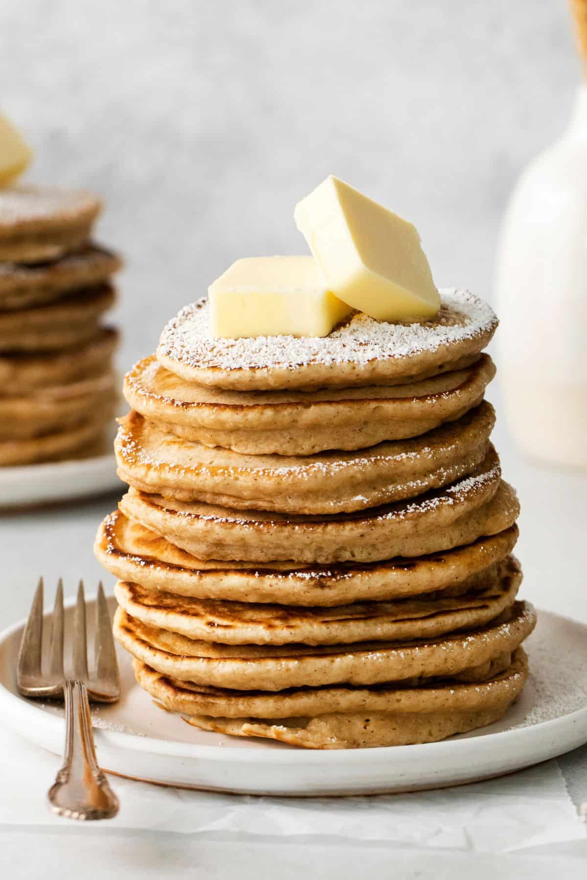 Stacked french toast pancakes on a plate with butter and powdered sugar on top.