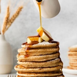 French toast pancakes stacked on a plate with butter on top and maple syrup being poured over top.