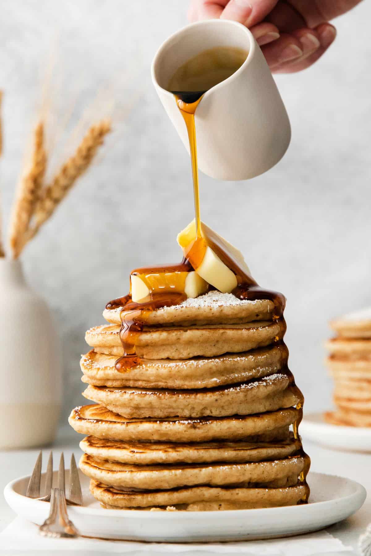 French toast pancakes stacked on a plate with butter on top and maple syrup being poured over top.