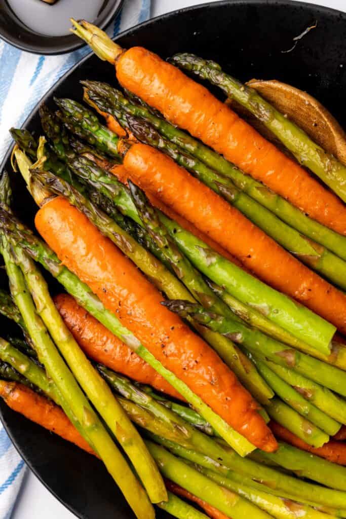 Close up of roasted carrots and asparagus on a black serving plate.