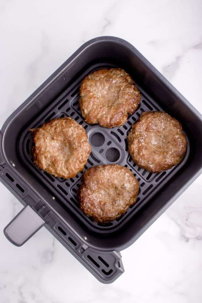 Cooked burgers in an air fryer basket.