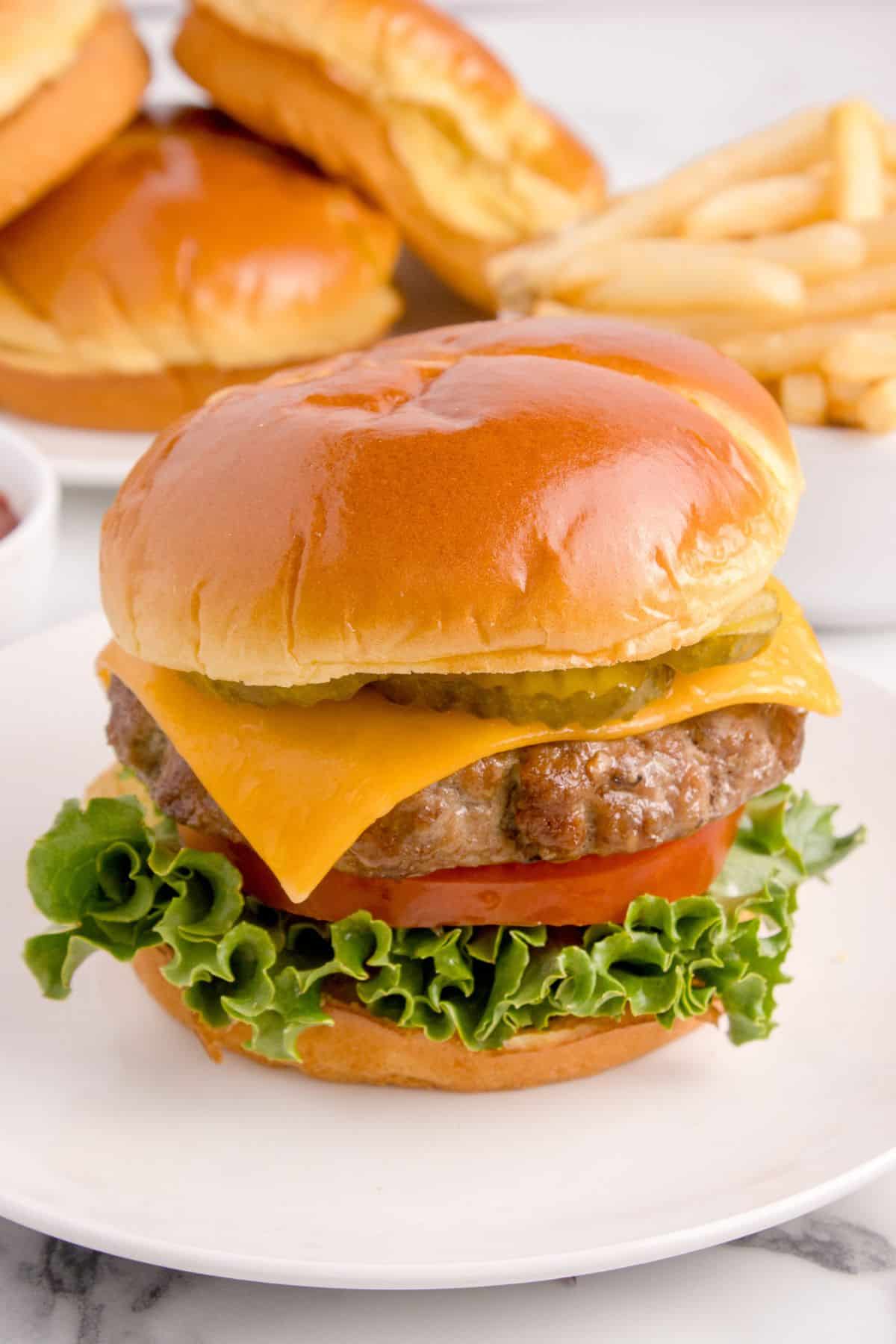 Air fryer hamburger on a white plate with a bun, cheese, lettuce, tomato, and pickles.
