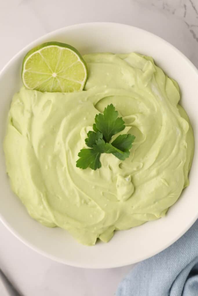 Overhead view of avocado crema with a fresh lime and piece of cilantro