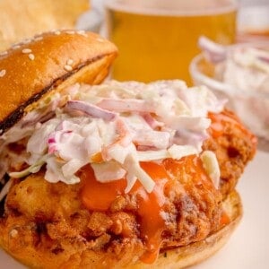 Buffalo chicken sandwich with coleslaw on top with the bun half on.