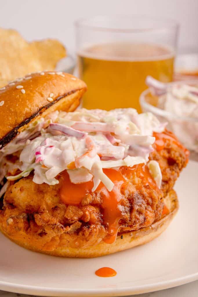 Buffalo chicken sandwich with coleslaw on top with the bun half on.